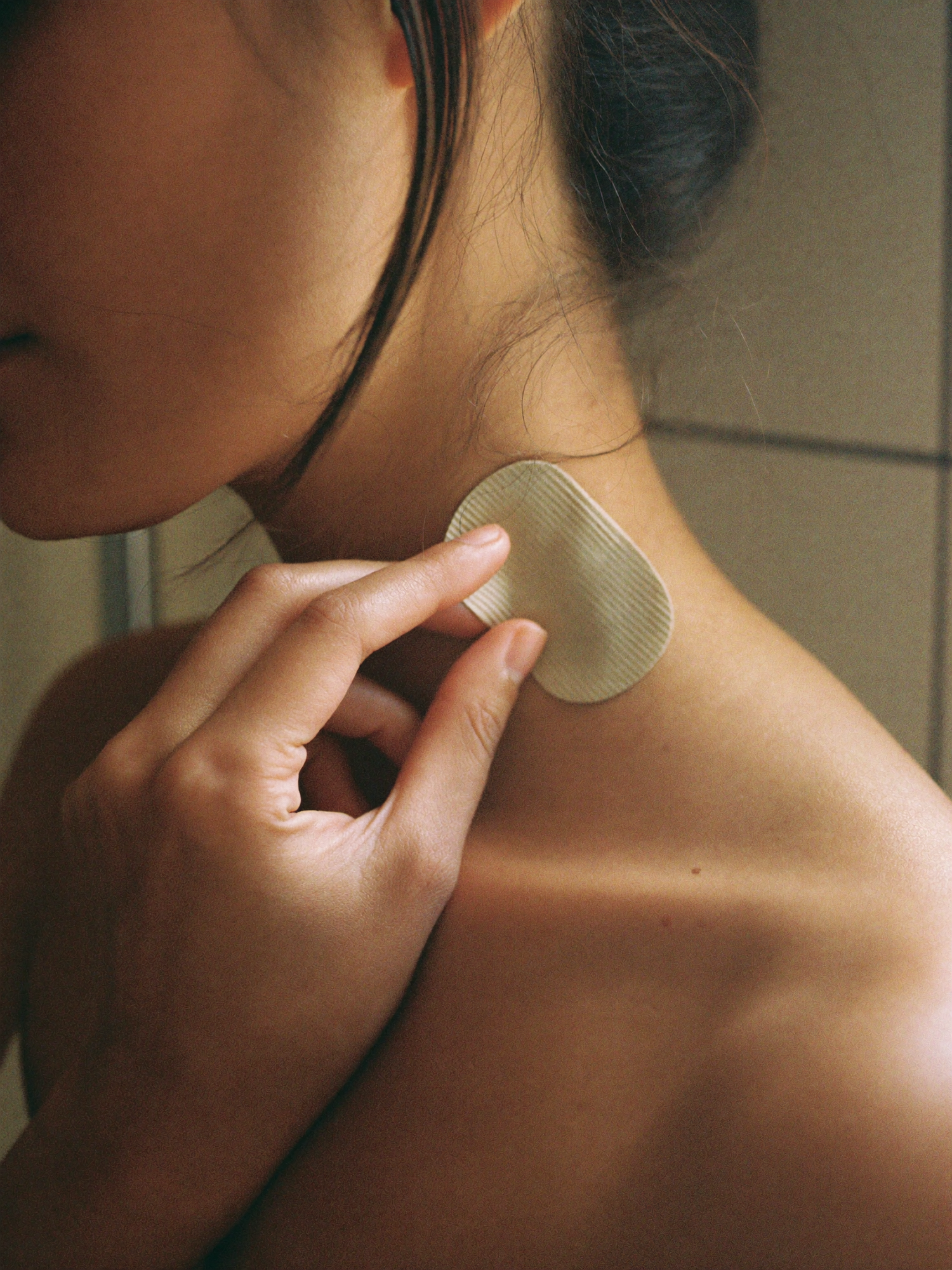 A hand gently pressing a discreet herbal patch onto the neck in soft morning light