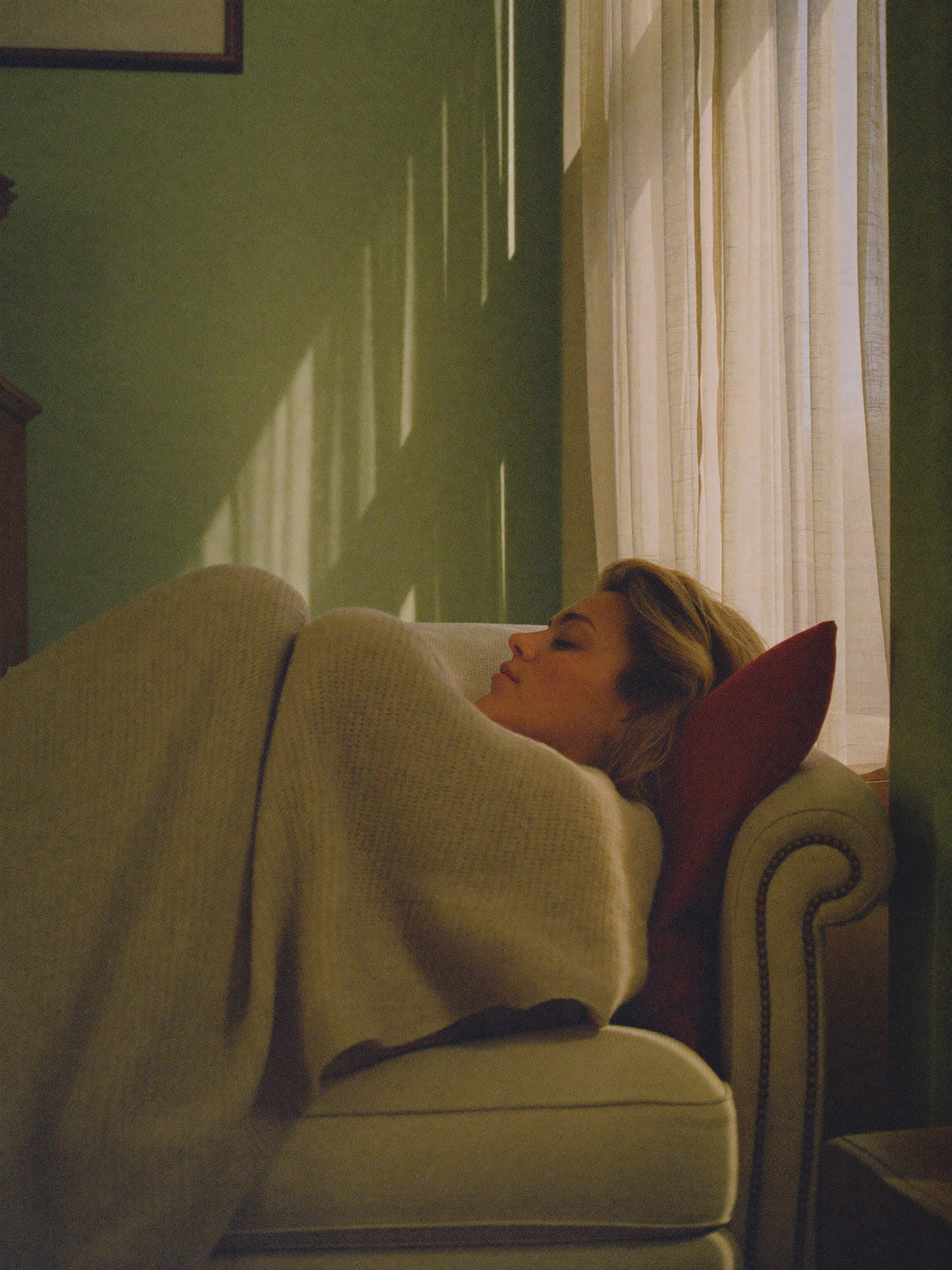 A woman unwinding in a reading corner wrapped in a knit blanket, golden hour light